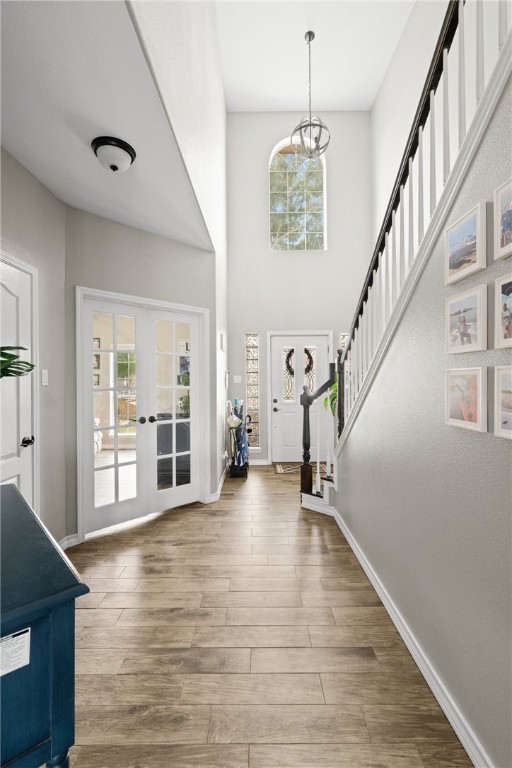 foyer with plenty of natural light, wood-type flooring, french doors, and a notable chandelier