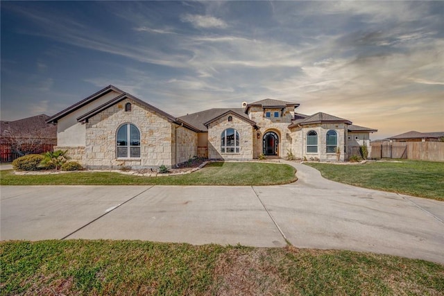 french country inspired facade with a front yard, fence, and stone siding