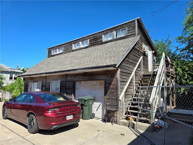 view of front of property featuring a shingled roof, concrete driveway, stairway, fence, and a garage