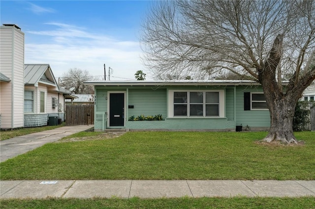 view of front of home with central AC unit, brick siding, fence, driveway, and a front lawn