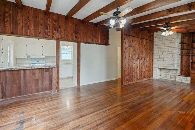 unfurnished living room featuring dark wood finished floors, ceiling fan, beamed ceiling, wood walls, and a sink