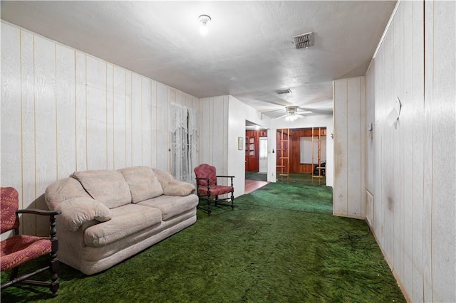 living room with wooden walls, carpet floors, a ceiling fan, and visible vents