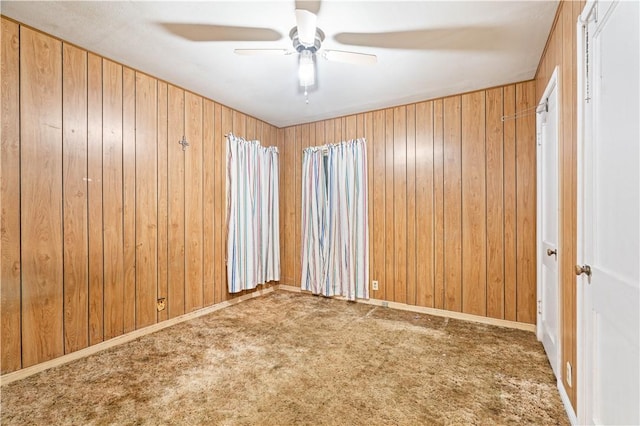 spare room featuring wooden walls, ceiling fan, and carpet flooring