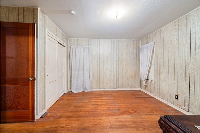 unfurnished room with baseboards, wood walls, and wood finished floors