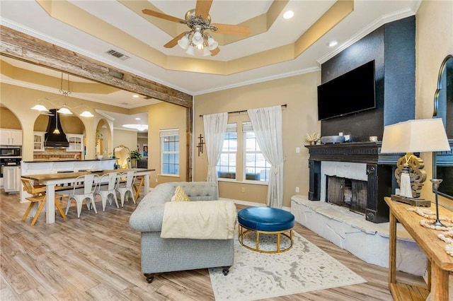 living area with a tray ceiling, a fireplace, crown molding, visible vents, and light wood-style floors