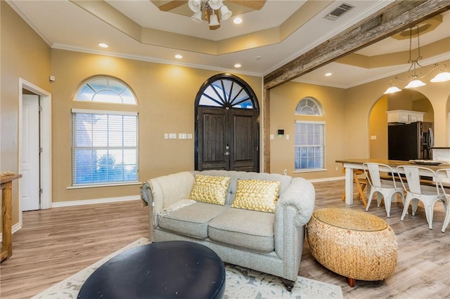 living room featuring light wood finished floors, visible vents, a raised ceiling, and arched walkways