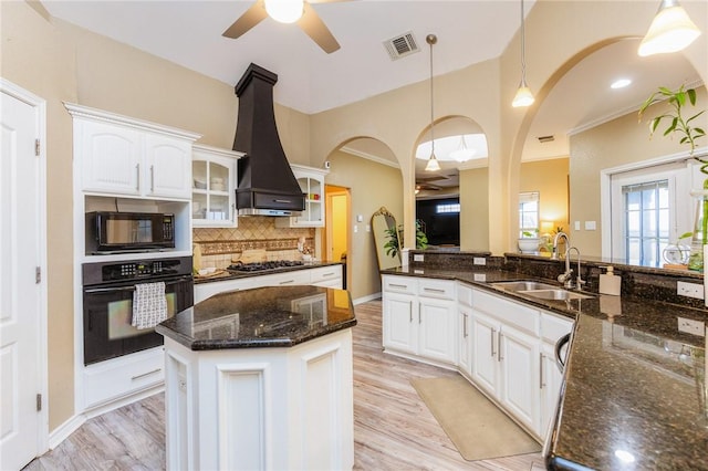 kitchen featuring tasteful backsplash, visible vents, black appliances, premium range hood, and a sink