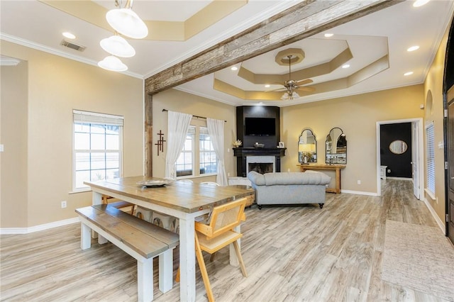 dining room featuring a large fireplace, visible vents, a raised ceiling, baseboards, and light wood-style flooring