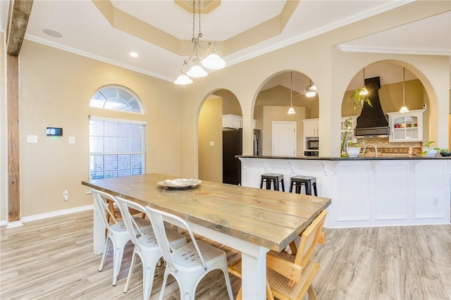 dining space with light wood-style floors, baseboards, ornamental molding, and a raised ceiling