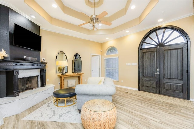 entryway with a fireplace with raised hearth, recessed lighting, wood finished floors, baseboards, and a tray ceiling