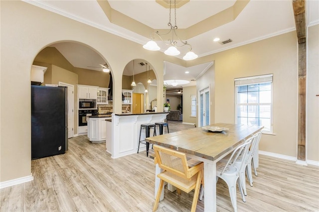 dining room featuring arched walkways, light wood finished floors, a raised ceiling, and baseboards