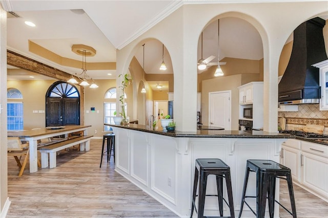 kitchen featuring a breakfast bar area, premium range hood, white cabinets, decorative backsplash, and built in microwave