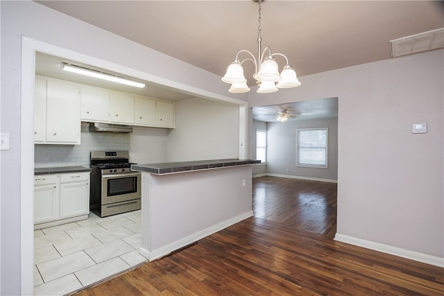 kitchen featuring stainless steel gas stove, decorative light fixtures, white cabinets, ceiling fan with notable chandelier, and light wood-type flooring