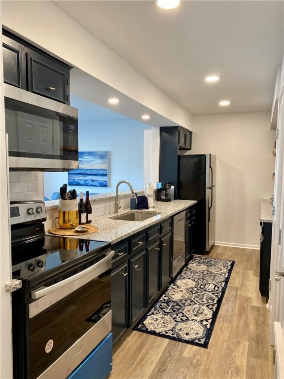 kitchen featuring stainless steel appliances, light stone counters, sink, backsplash, and light hardwood / wood-style flooring