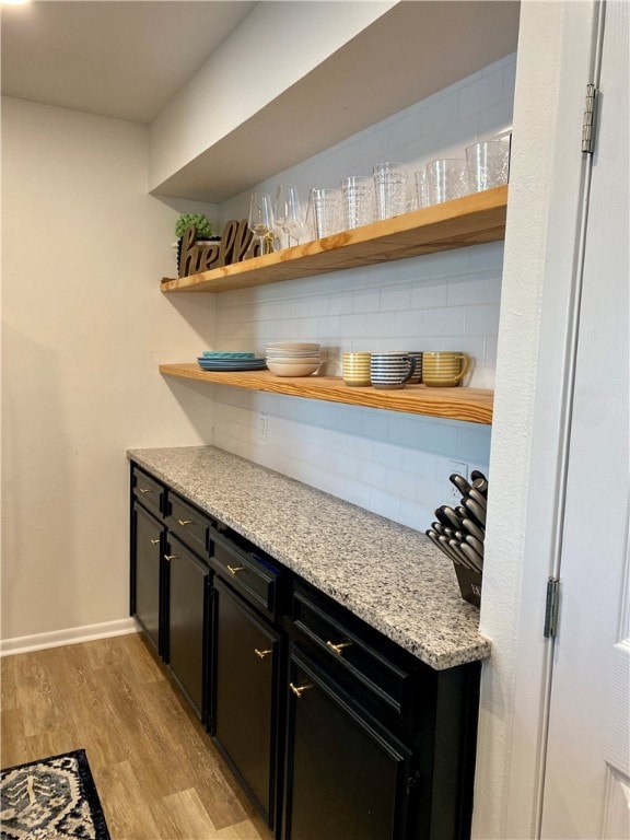 bar featuring decorative backsplash, light hardwood / wood-style flooring, and light stone counters