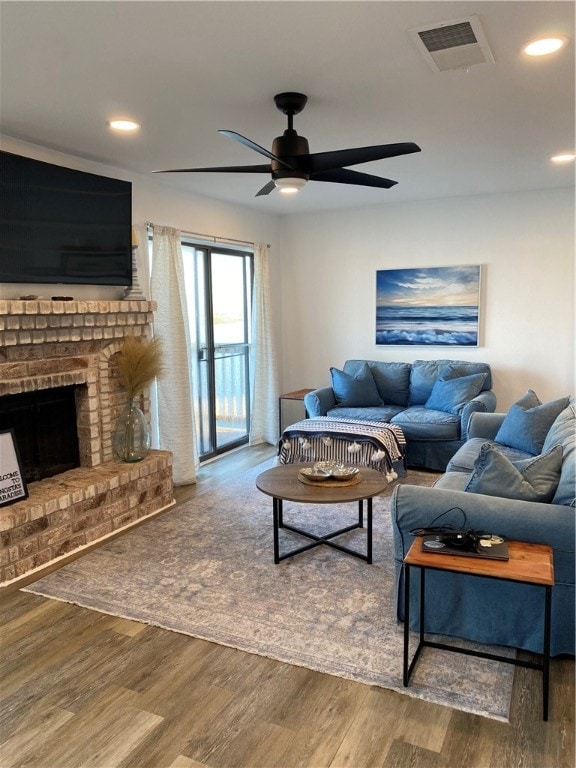 living room featuring a brick fireplace, wood-type flooring, and ceiling fan