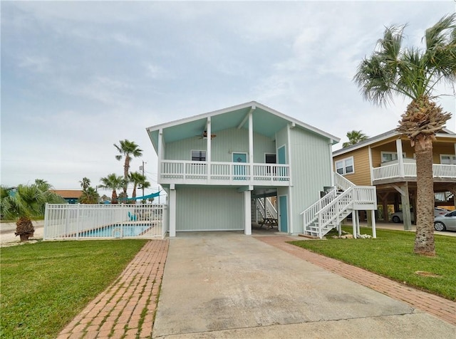 back of house featuring driveway, a carport, ceiling fan, stairs, and a balcony