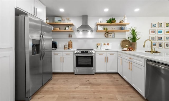 kitchen featuring wall chimney range hood, sink, light hardwood / wood-style flooring, white cabinetry, and stainless steel appliances