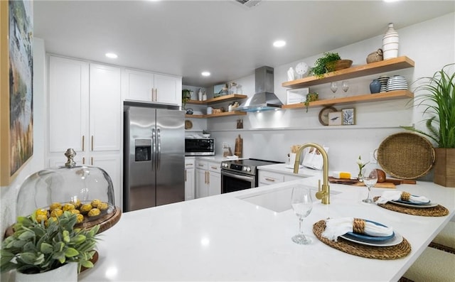 kitchen featuring wall chimney range hood, sink, white cabinetry, kitchen peninsula, and stainless steel appliances