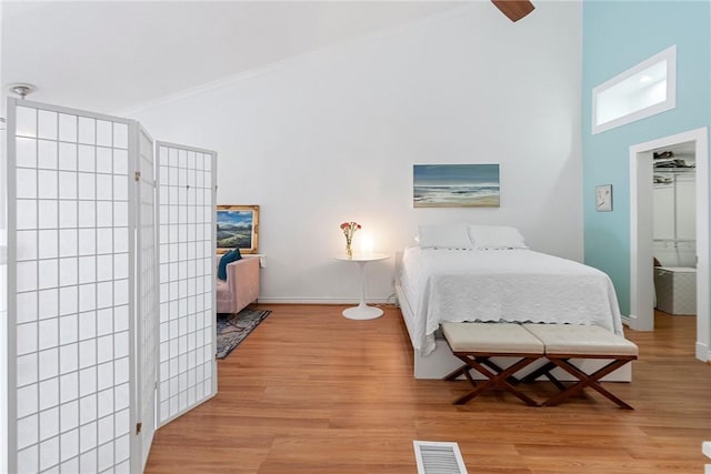 bedroom with a high ceiling, light hardwood / wood-style floors, ceiling fan, and ornamental molding