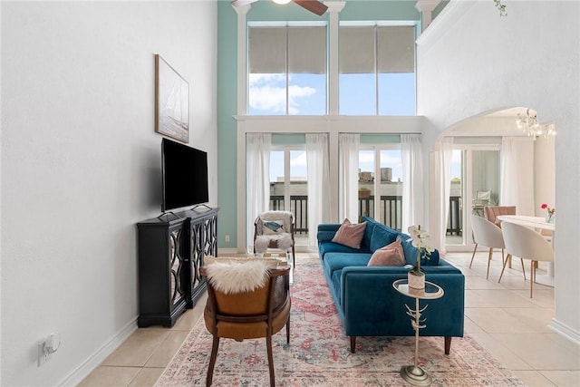 tiled living room featuring ceiling fan with notable chandelier and a high ceiling