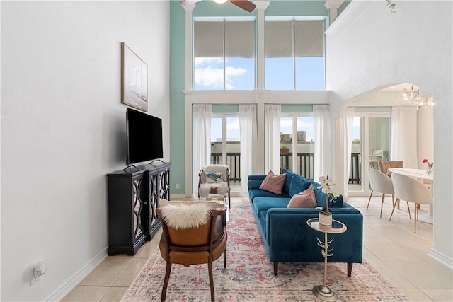 living room featuring ceiling fan with notable chandelier, light tile patterned floors, and a high ceiling