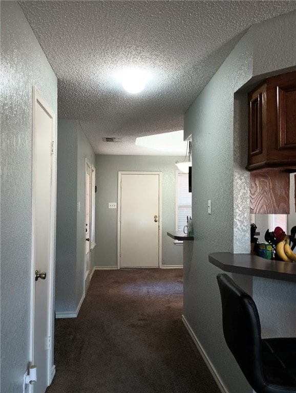 hallway with a textured ceiling and dark carpet