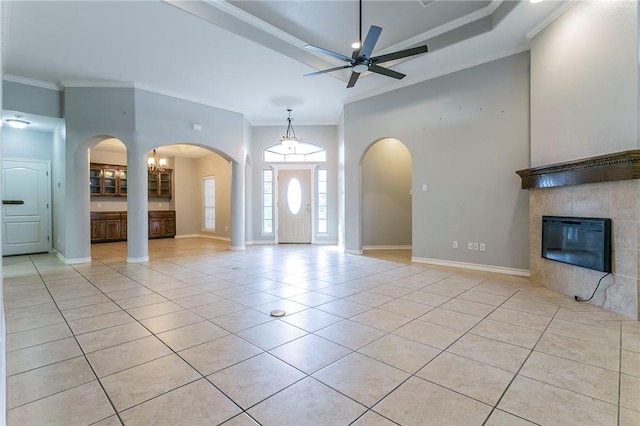 tiled entryway featuring a tile fireplace, a high ceiling, ceiling fan with notable chandelier, and ornamental molding