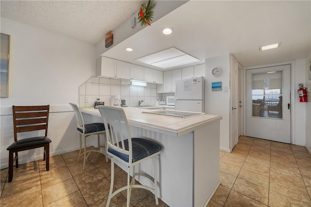 kitchen featuring backsplash, kitchen peninsula, tile countertops, white appliances, and white cabinets