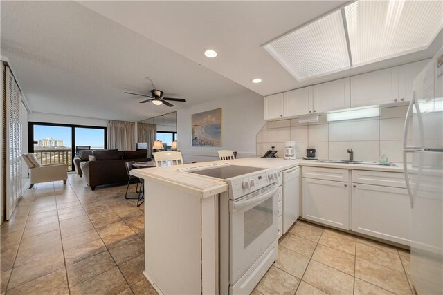 kitchen featuring white appliances, white cabinets, backsplash, kitchen peninsula, and ceiling fan