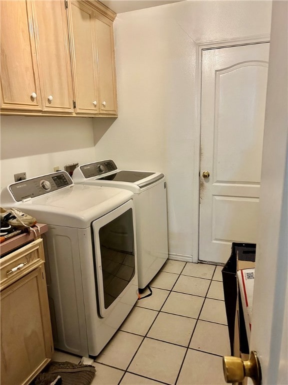 clothes washing area with washing machine and dryer, cabinets, and light tile patterned floors