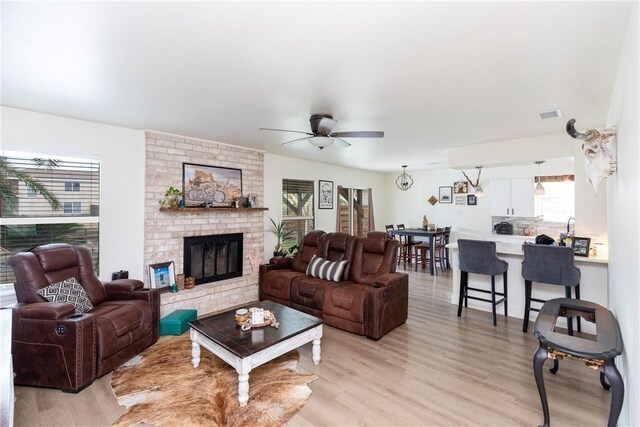 living room with ceiling fan, light wood-type flooring, and a brick fireplace