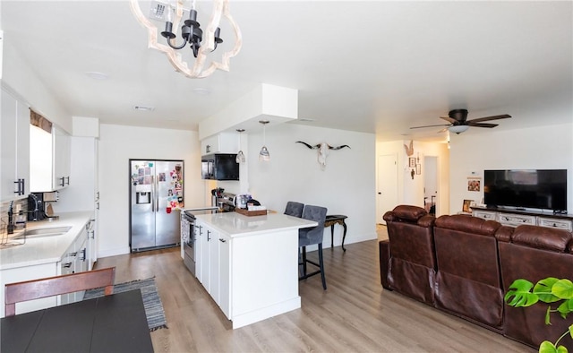 kitchen featuring sink, white cabinetry, hanging light fixtures, appliances with stainless steel finishes, and a kitchen breakfast bar