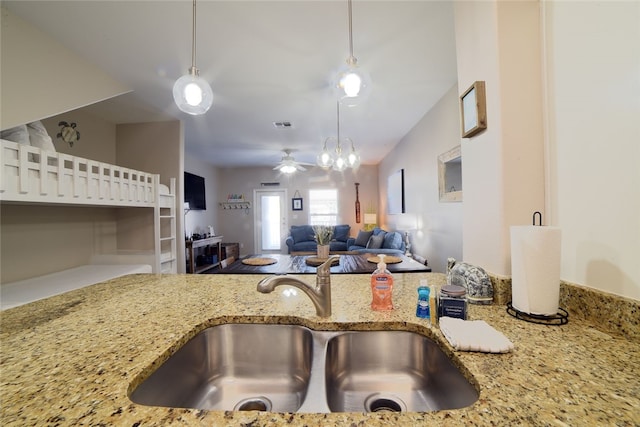 kitchen with pendant lighting, ceiling fan, light stone countertops, and sink