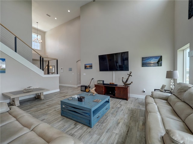 living room featuring a towering ceiling, light hardwood / wood-style flooring, and a notable chandelier