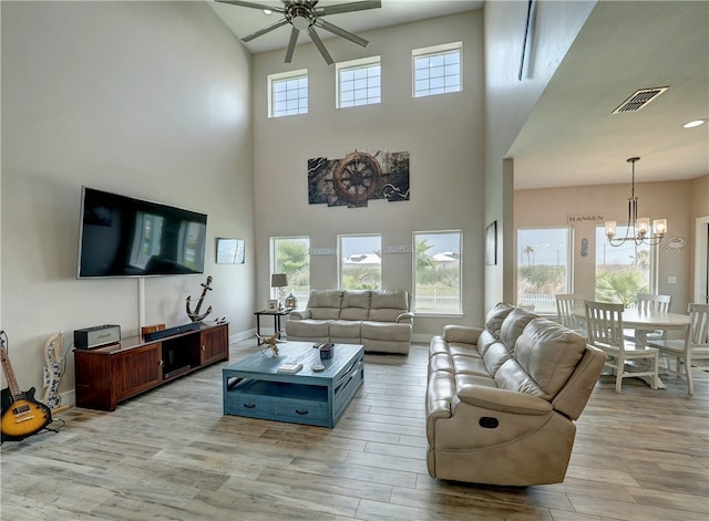 living room with a towering ceiling, ceiling fan with notable chandelier, and light hardwood / wood-style flooring