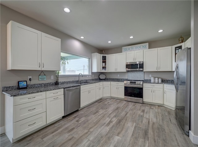 kitchen with white cabinets, stainless steel appliances, light hardwood / wood-style flooring, and dark stone countertops