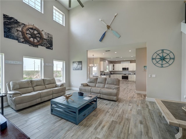 living room with ceiling fan with notable chandelier, a towering ceiling, and light hardwood / wood-style floors