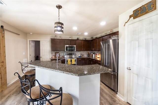 11766 Fm 70, Robstown, TX 78380 - kitchen with stainless steel appliances, dark brown cabinetry, light wood-style floors, a barn door, and a breakfast bar area
