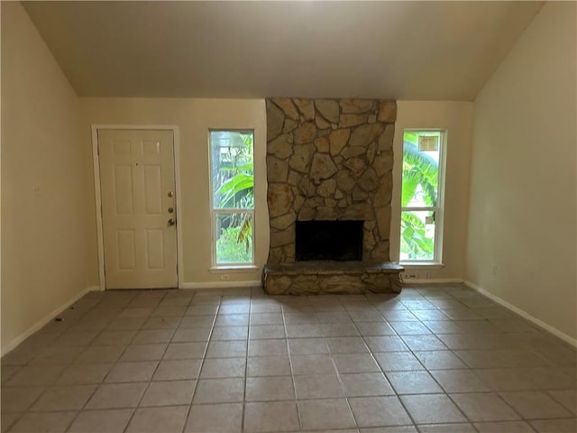 unfurnished living room featuring lofted ceiling, light tile patterned floors, and a stone fireplace