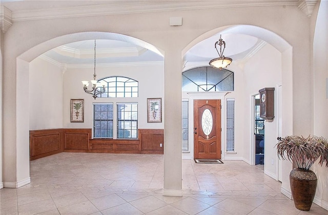 foyer with ornamental molding, a wealth of natural light, wainscoting, and a notable chandelier