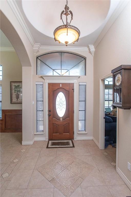 entryway featuring arched walkways, a high ceiling, ornamental molding, light tile patterned flooring, and baseboards