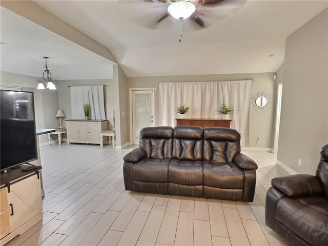 living room featuring lofted ceiling, light wood-style flooring, baseboards, and ceiling fan with notable chandelier