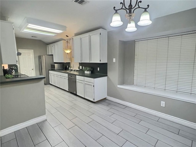 kitchen featuring dark countertops, appliances with stainless steel finishes, white cabinets, and decorative light fixtures