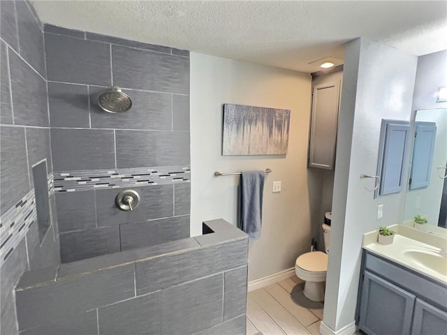 bathroom with a textured ceiling, toilet, wood finish floors, vanity, and tiled shower