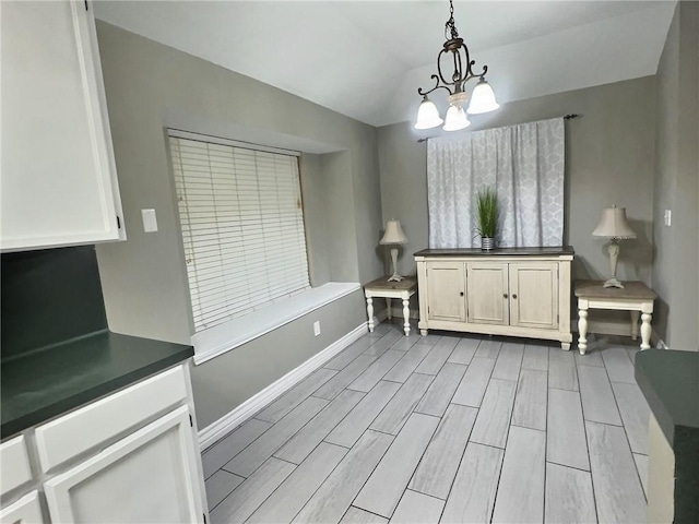 unfurnished dining area with lofted ceiling, baseboards, a chandelier, and wood finish floors