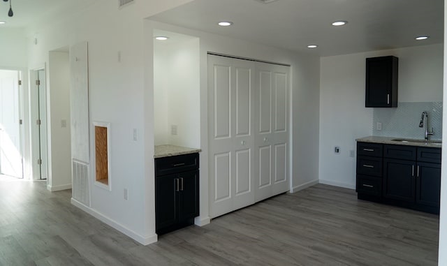 kitchen with sink, decorative backsplash, light hardwood / wood-style flooring, and light stone countertops