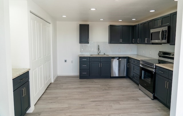 kitchen with sink, light wood-type flooring, stainless steel appliances, light stone countertops, and decorative backsplash