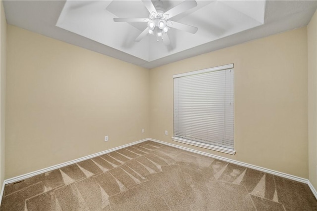 carpeted spare room with a raised ceiling, baseboards, and ceiling fan