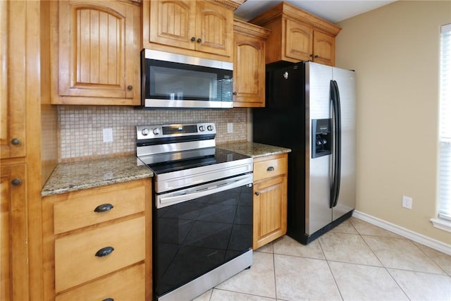 kitchen with light tile patterned floors, baseboards, light stone counters, stainless steel appliances, and backsplash